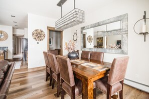 A dining area with a wooden table, leather chairs, a vase with flowers, and a large mirror on the wall.