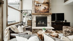 Una sala de estar con chimenea de piedra, sofá de cuero y televisor grande.