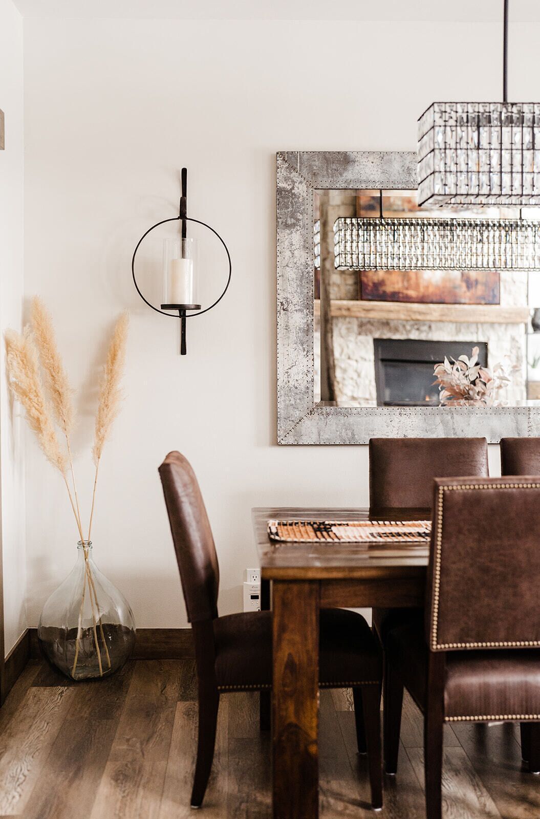 A dining area with a wooden table, leather chairs, a wall-mounted light fixture, and a framed picture of a fireplace.