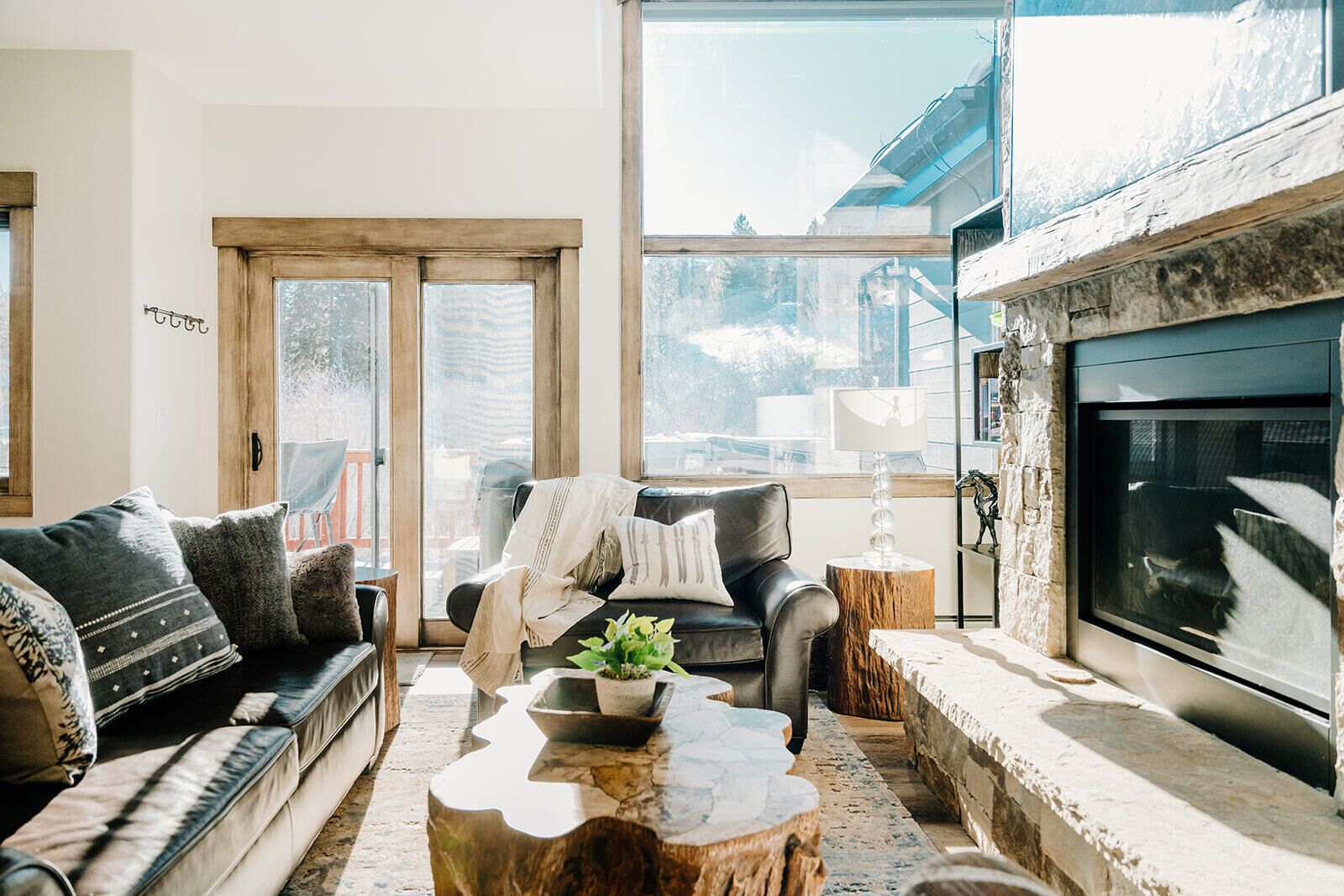Ein gemütliches Wohnzimmer mit Kamin, einer Couch, einem Couchtisch und einem großen Fenster mit Blick ins Freie.