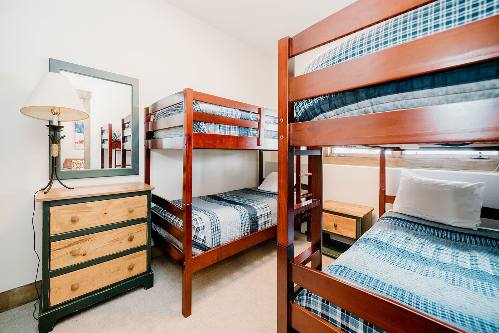 A room with bunk beds, a wooden dresser with drawers, a lamp, and a mirror.