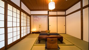 Um quarto japonês tradicional com tatames, uma mesa baixa, uma cadeira, um candeeiro pendente e portas deslizantes.