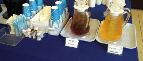 Una mesa de buffet con diversas opciones de comida y bebida, incluyendo jugo de manzana y una jarra de té helado.