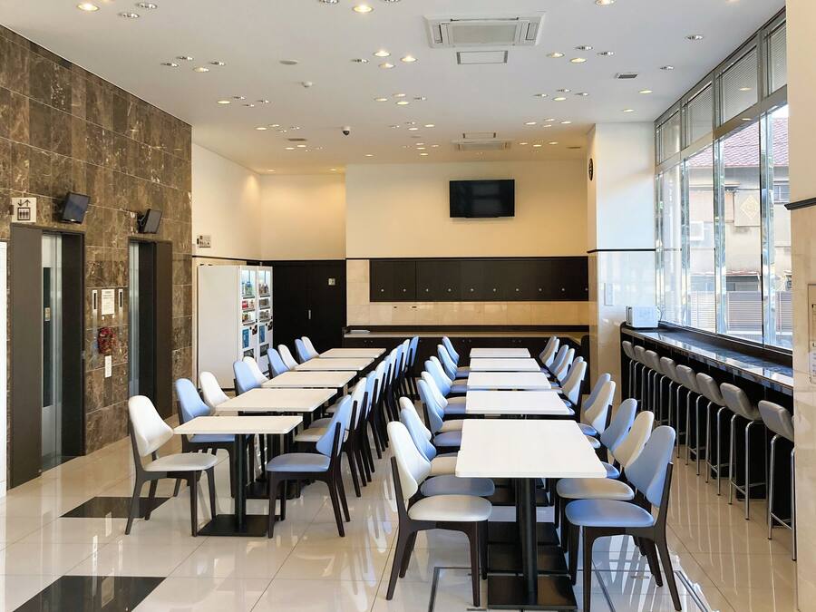 A modern conference room with long tables and chairs, a large flat-screen TV, and a vending machine.