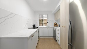 Cuina moderna amb armaris blancs, nevera d'acer inoxidable i finestra amb vista a l'exterior.