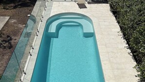 Una piscina rectangular amb aigua blava cristal·lina, envoltada per un solàrium amb rajoles i una zona verda.
