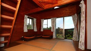 Une cabane en bois avec des tatamis, un lit en mezzanine et une porte-fenêtre coulissante donnant sur un jardin.