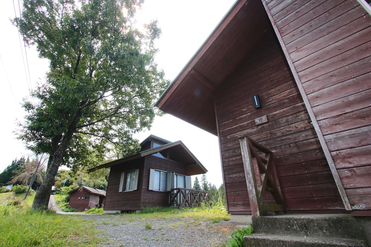 A rustic wooden cabin with a sloped roof, a small porch, and a gravel driveway.