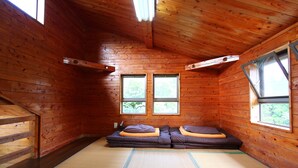 Une pièce de cabane en bois avec un sol recouvert de tatamis, deux fenêtres et un canapé avec des coussins.