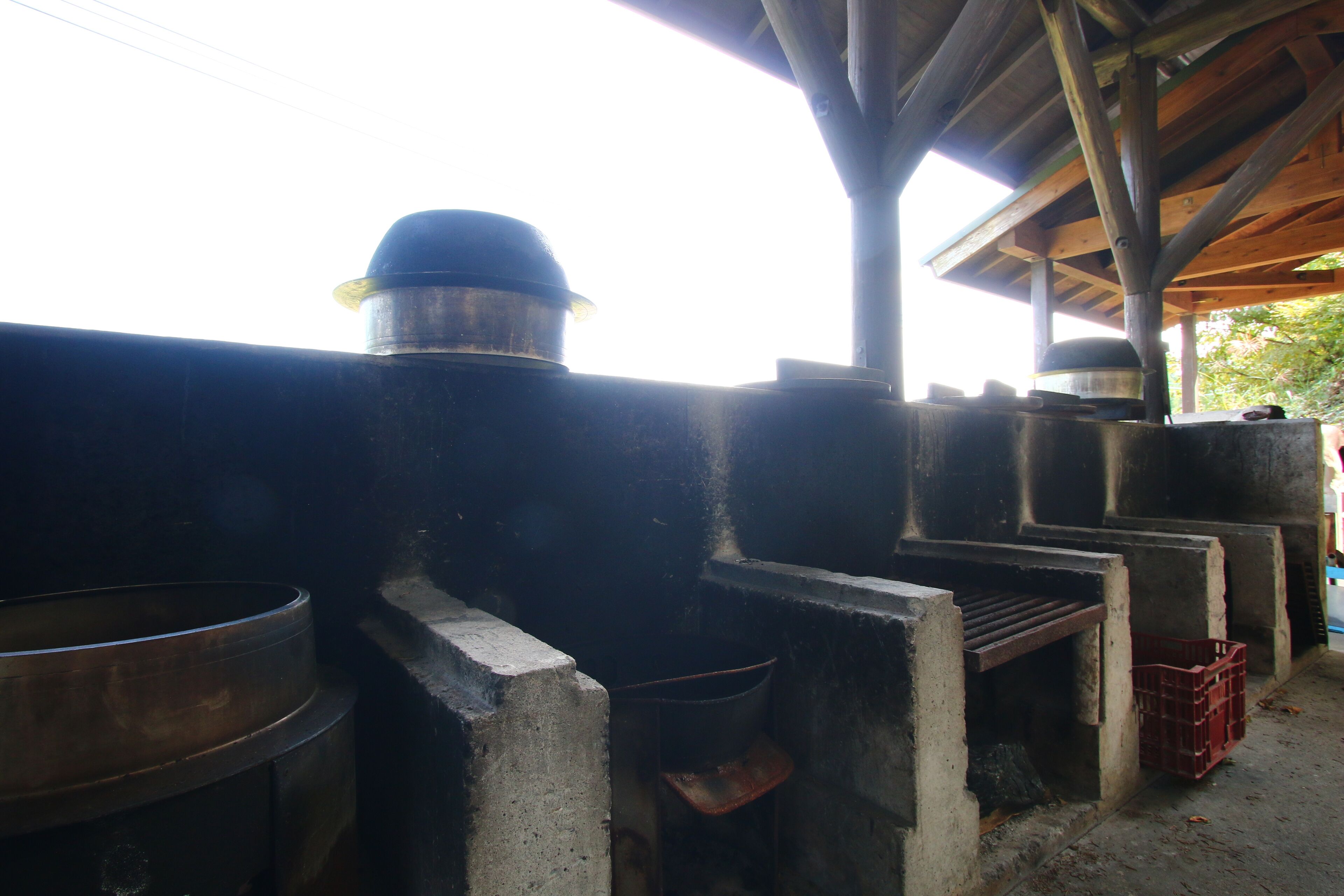 A series of large industrial cooking pots under a covered structure.