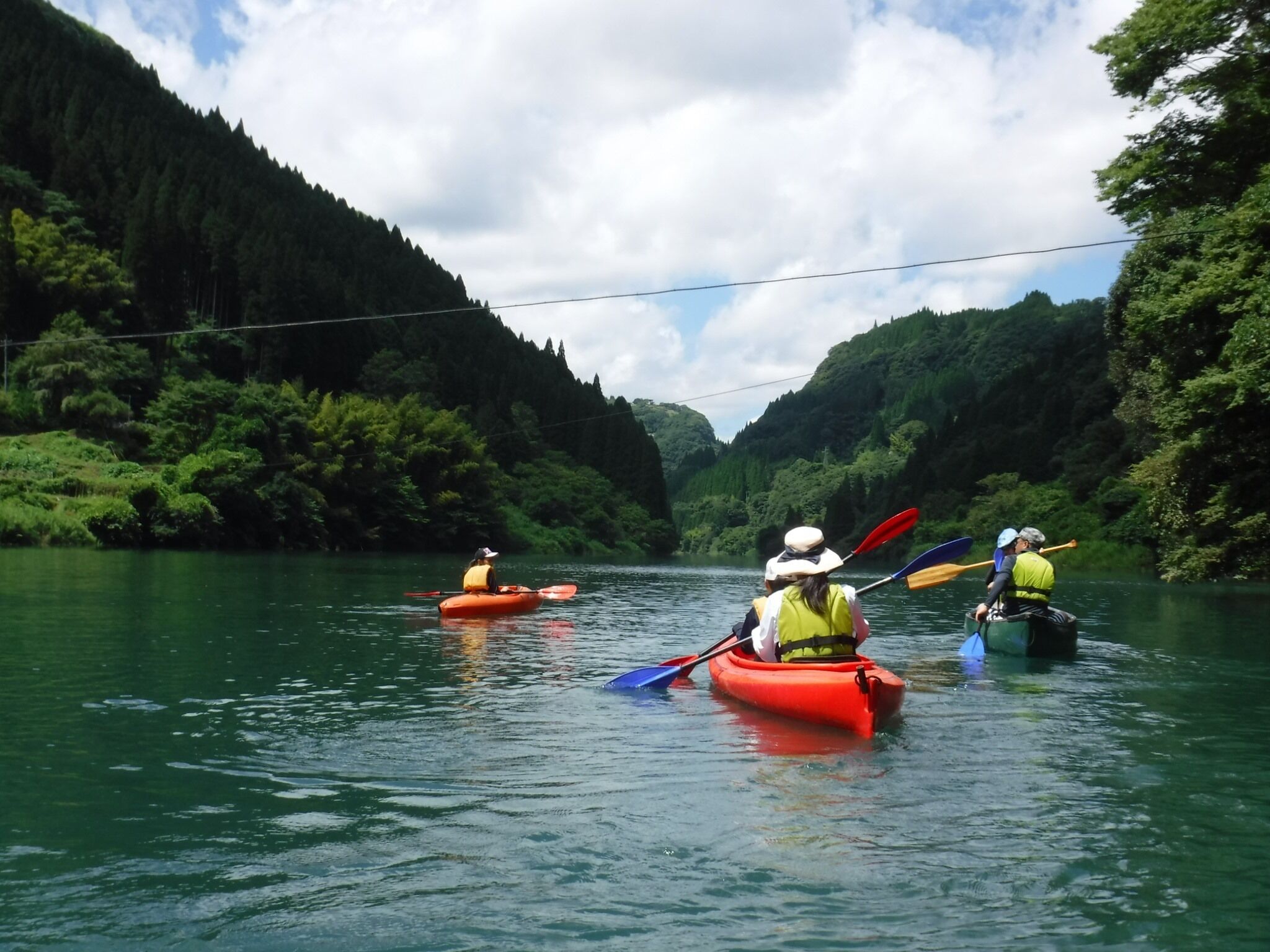 Drei Kanuten auf einem ruhigen Fluss, umgeben von dichtem Wald.