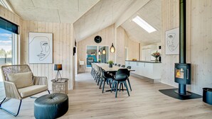 A spacious, modern interior with a wooden interior, a dining area with a long table and chairs, a kitchen with a stove, and a large window providing natural light. - Lovely home in Nørre Nebel with sauna (Nørre Nebel)