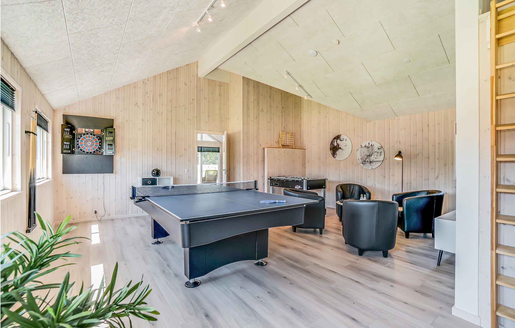 Un espacio interior moderno con mesa de ping-pong, zona de estar, dardos y mesa de fútbol de mesa.