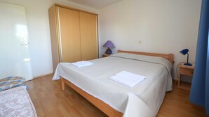 Un dormitorio con cama, armario, mesita de noche con lámpara y una lámpara azul sobre una mesita auxiliar.