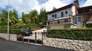 Un edificio residencial de dos plantas con un muro de piedra y una verja metálica.