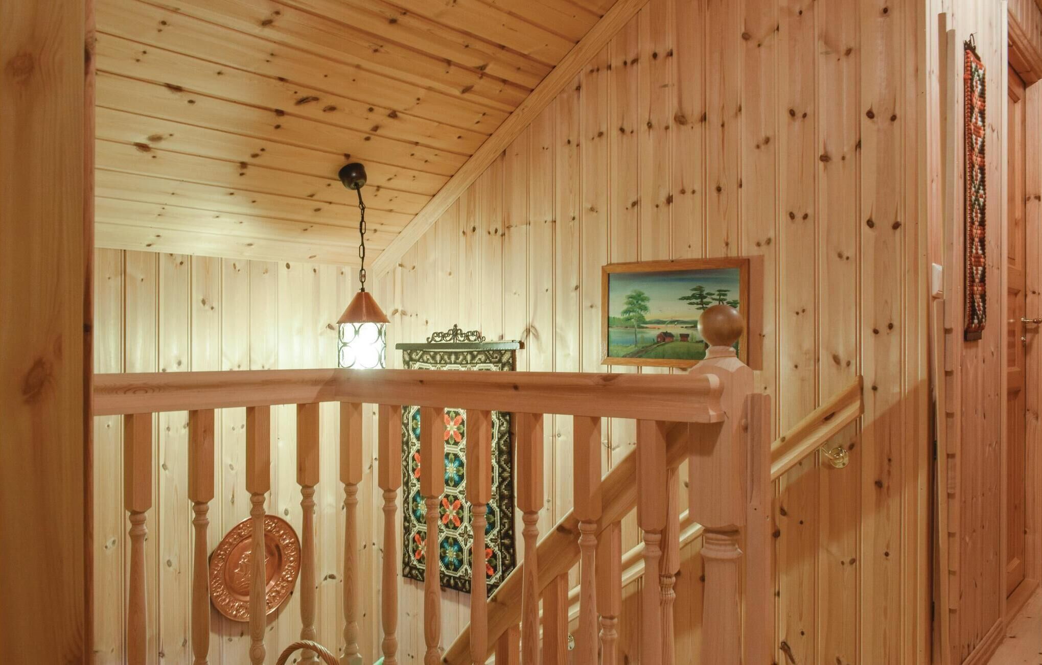 A wooden interior with a staircase, a hanging lantern, and a painting on the wall.