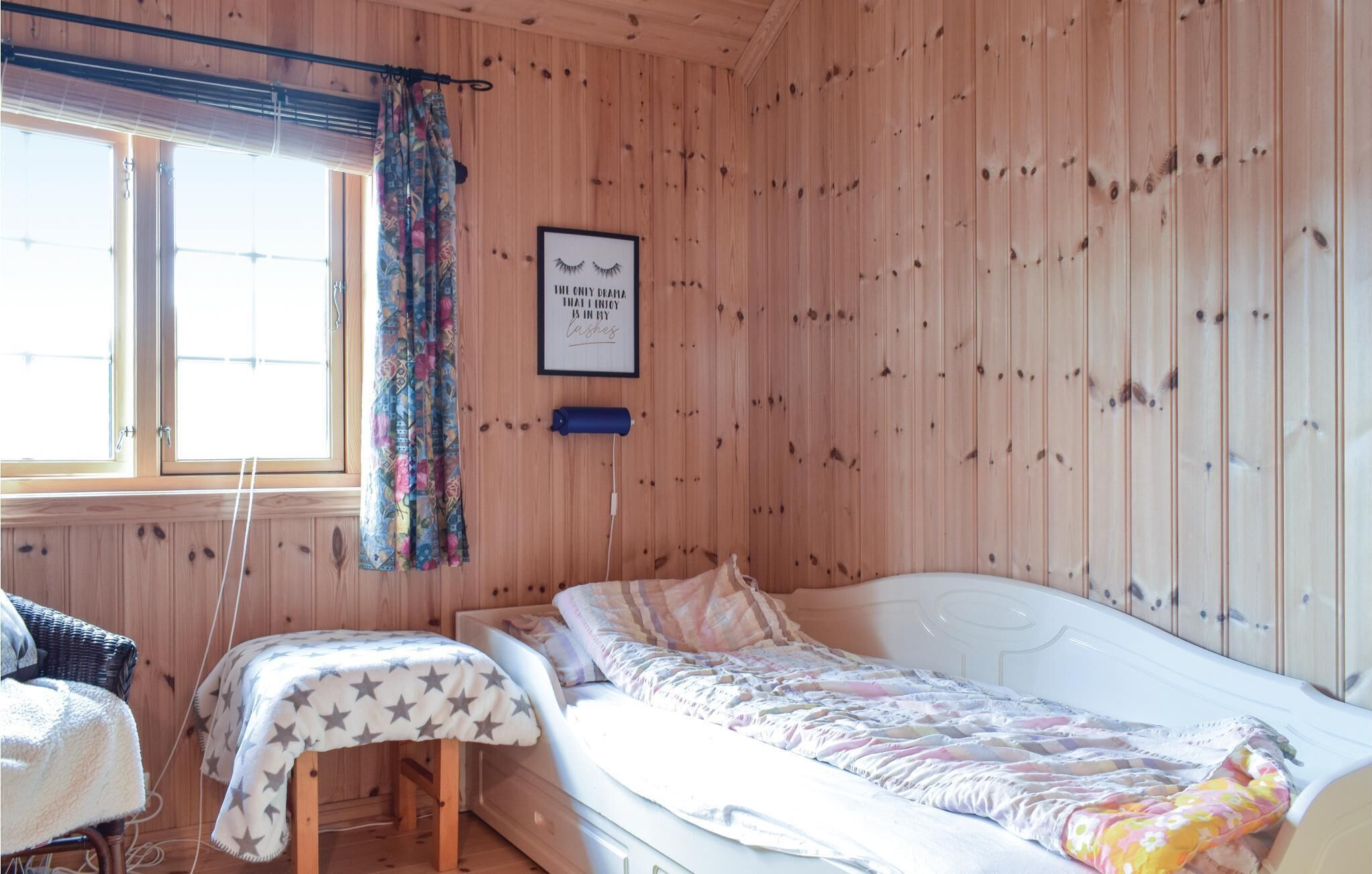 Ein kleiner, gemütlicher Raum mit Holzwänden, einem Einzelbett, einem kleinen Tisch und einem Fenster mit Vorhängen.