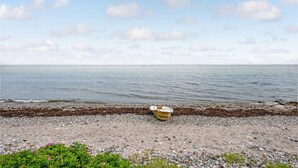 Ein Strand mit einem kleinen Boot am Ufer, felsigem Ufer und ruhigem Meer unter einem teils bewölkten Himmel.