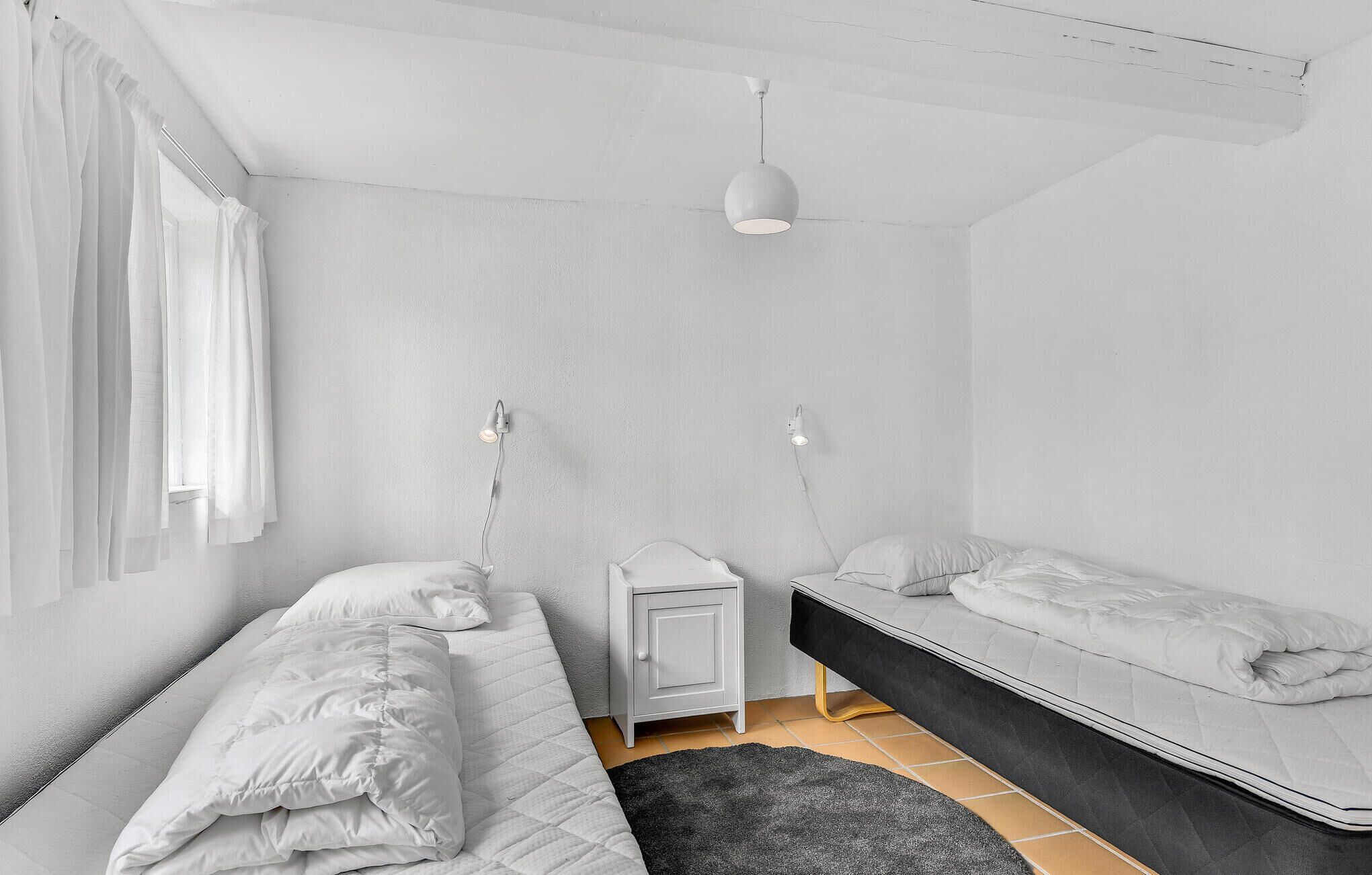 Une chambre à coucher au style minimaliste, avec deux lits, une table de chevet et une lampe suspendue.