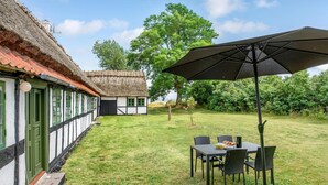 Ein traditionelles Fachwerkhäuschen mit Strohdach, ein kleiner Garten mit Tisch und Stühlen sowie ein großer Sonnenschirm.