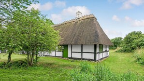 Ein traditionelles Reetdachhaus mit weißer und dunkler Fachwerkbauweise, umgeben von einer grasbewachsenen Wiese und Bäumen.
