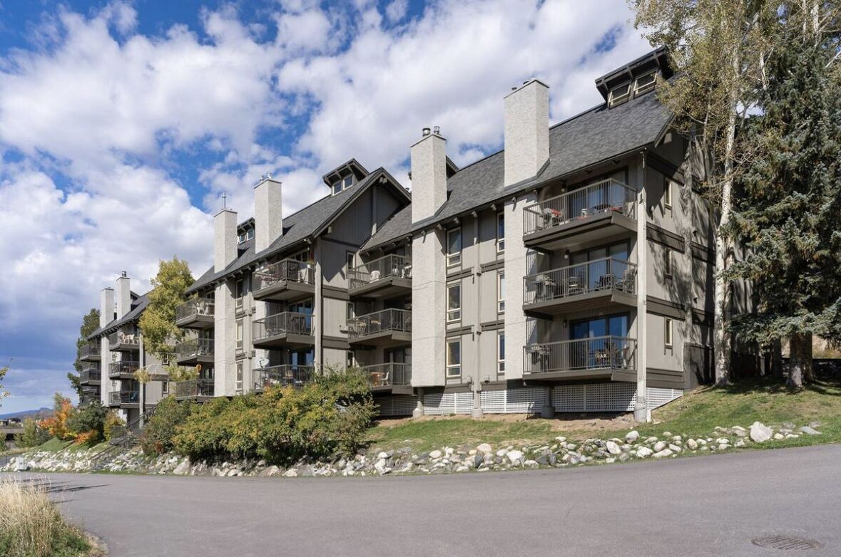Un immeuble résidentiel à plusieurs étages, doté de balcons, d’une façade en pierre et d’un jardin paysager à l’avant.