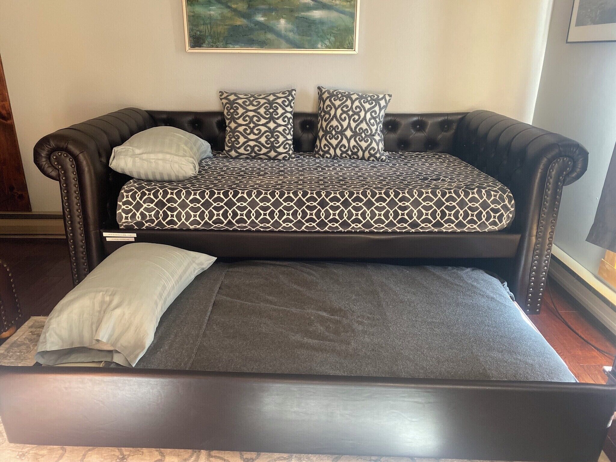 Un canapé-lit marron foncé, recouvert d’un tissu à motifs, avec deux coussins.