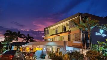 A hotel with a two-story structure, a covered outdoor seating area, and a car parked in front.