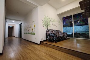 A hallway with a wooden floor, a wall with a tree mural, and a couch with a floral pattern. - Treeline Urban Inn (Kota Kinabalu)