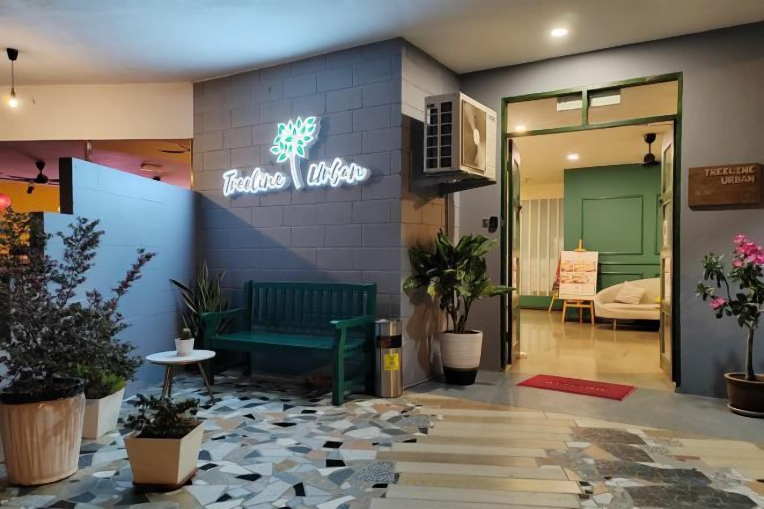 A hotel entrance with a neon sign, a reception desk, a green sofa, and potted plants.