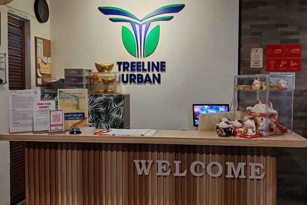 A reception desk with a 'WELCOME' sign, a logo for 'TREELINE URBAN', and various informational materials. - Treeline Urban Inn (Kota Kinabalu)