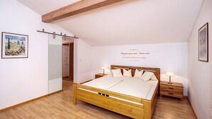A bedroom with a wooden bed, bedside tables, a wardrobe, and a painting on the wall. - Ferienwohnung für 4 Personen, 2 Schlafzimmer, 70 m² (Inzell)