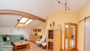 A cozy living room with a green sofa, a wooden coffee table, a white chair, and a cabinet with glass doors. There is a skylight above the sofa and a door leading to another room. - Ferienwohnung für 4 Personen, 2 Schlafzimmer, 70 m² (Inzell)
