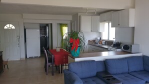 Une cuisine moderne avec des meubles blancs, un coin repas doté d’une table et de chaises rouges, et un canapé bleu dans le salon.
