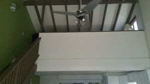 Un ventilateur de plafond dans une pièce dotée d’un plafond haut et de poutres en bois.
