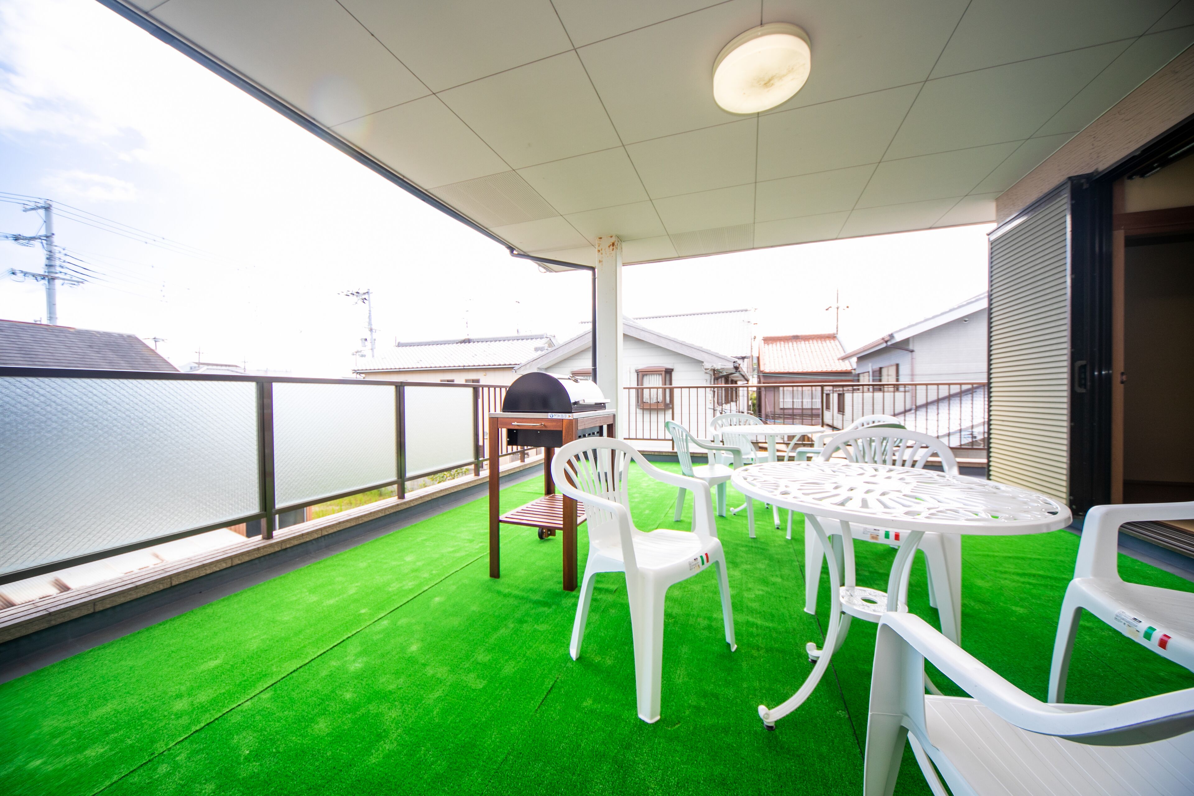 A covered outdoor area with artificial green flooring, white plastic chairs, and tables.