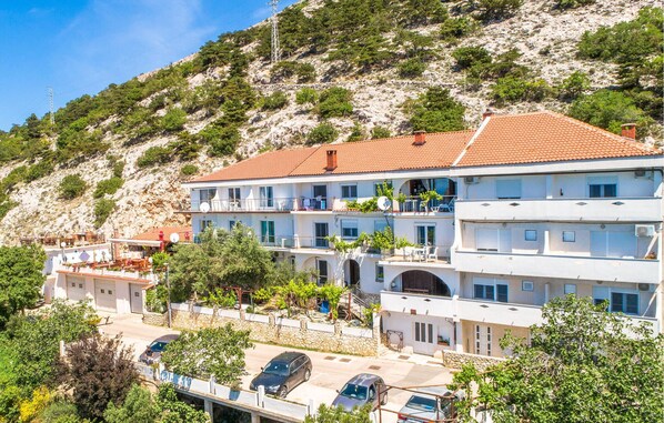 A multi-story hotel with balconies, a stone wall, and a hillside backdrop. - Beach front apartment in Stara Baska with WiFi (Stara Baska)
