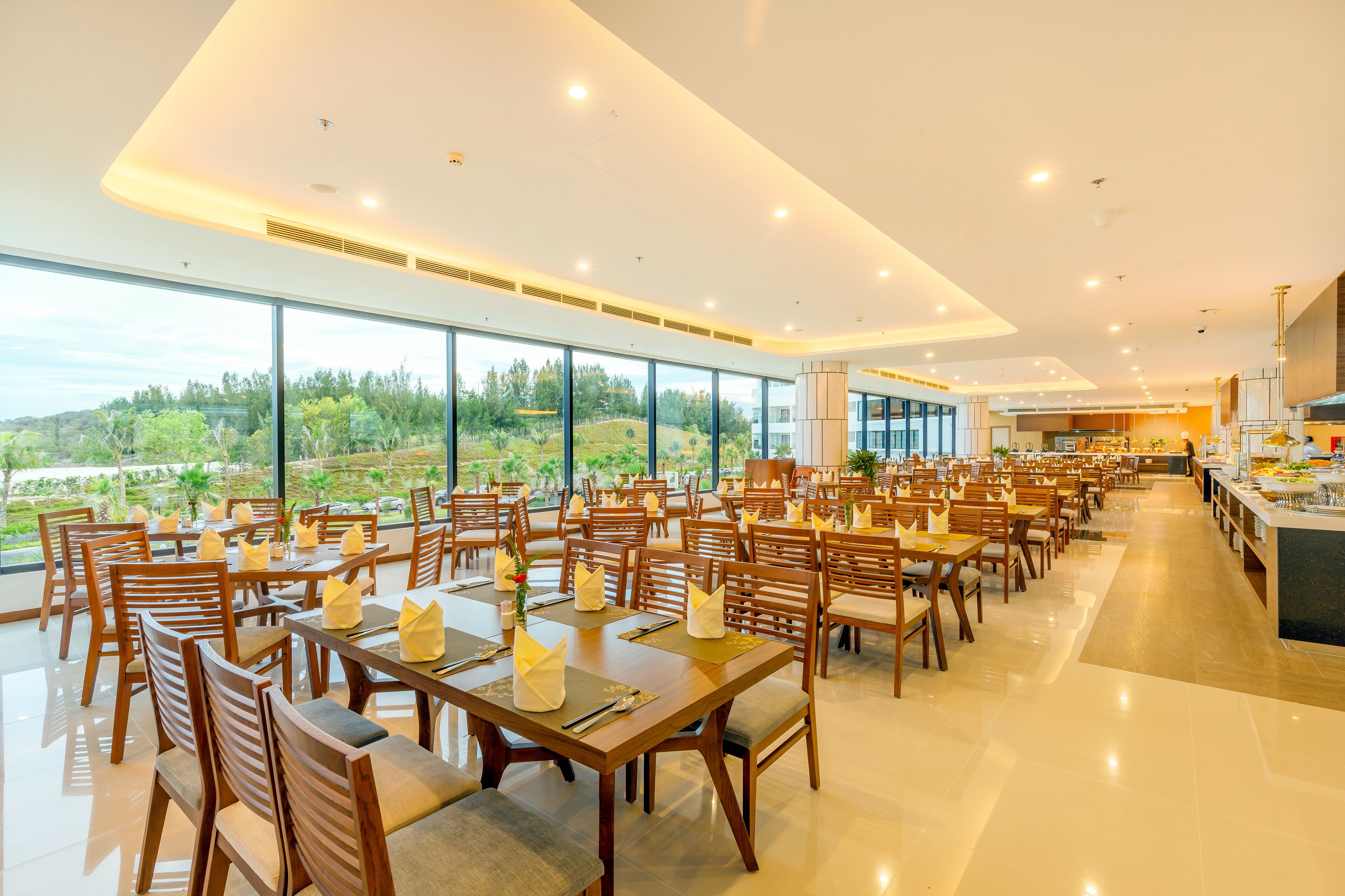 A spacious dining area with multiple tables and chairs, large windows offering a view of the outdoors, and a modern interior design.
