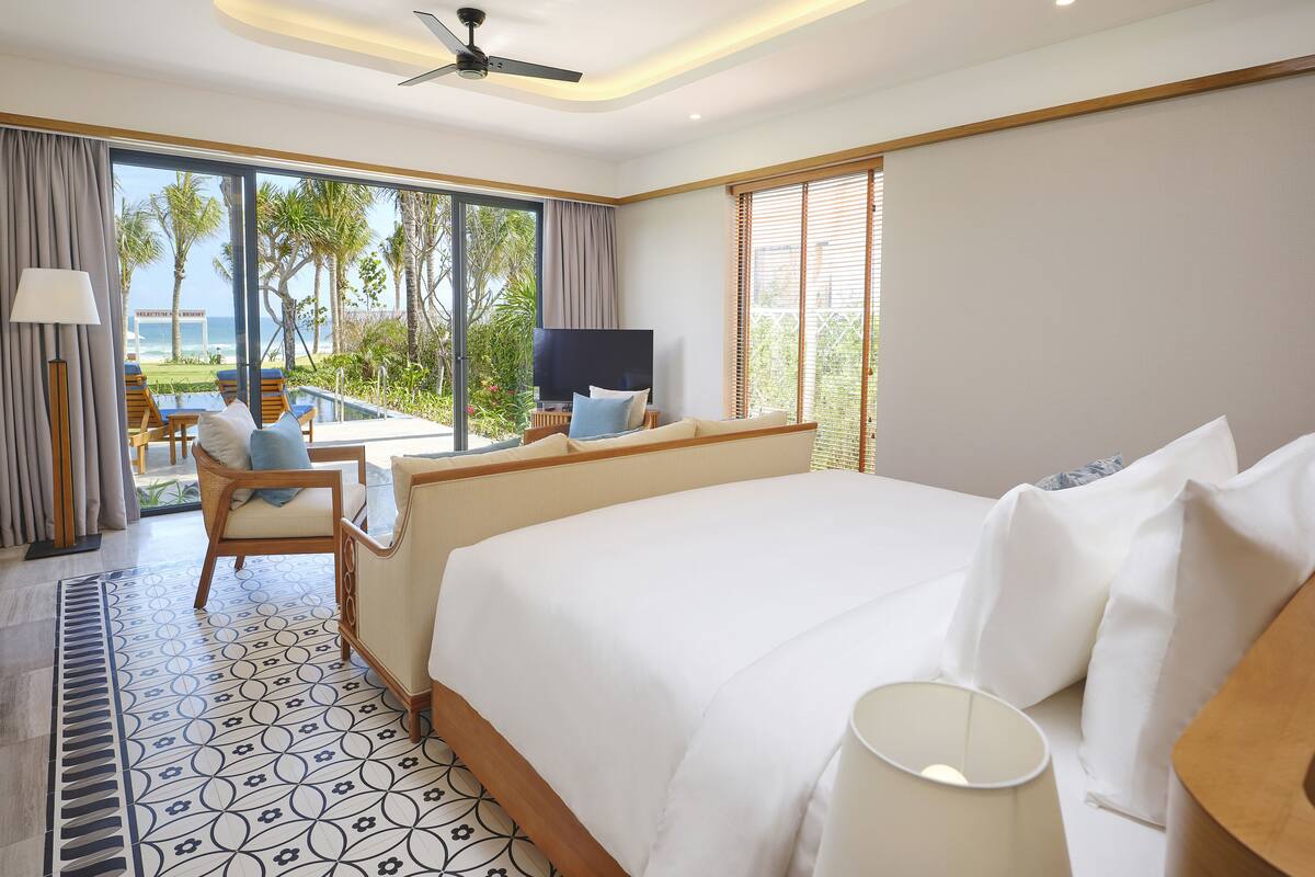 Une chambre d’hôtel avec un lit, une télévision, un balcon donnant sur une piscine et une vue sur l’océan.