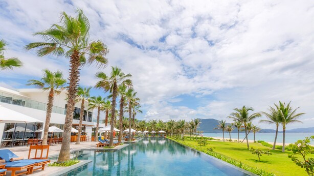 A poolside area with palm trees, lounge chairs, and umbrellas.