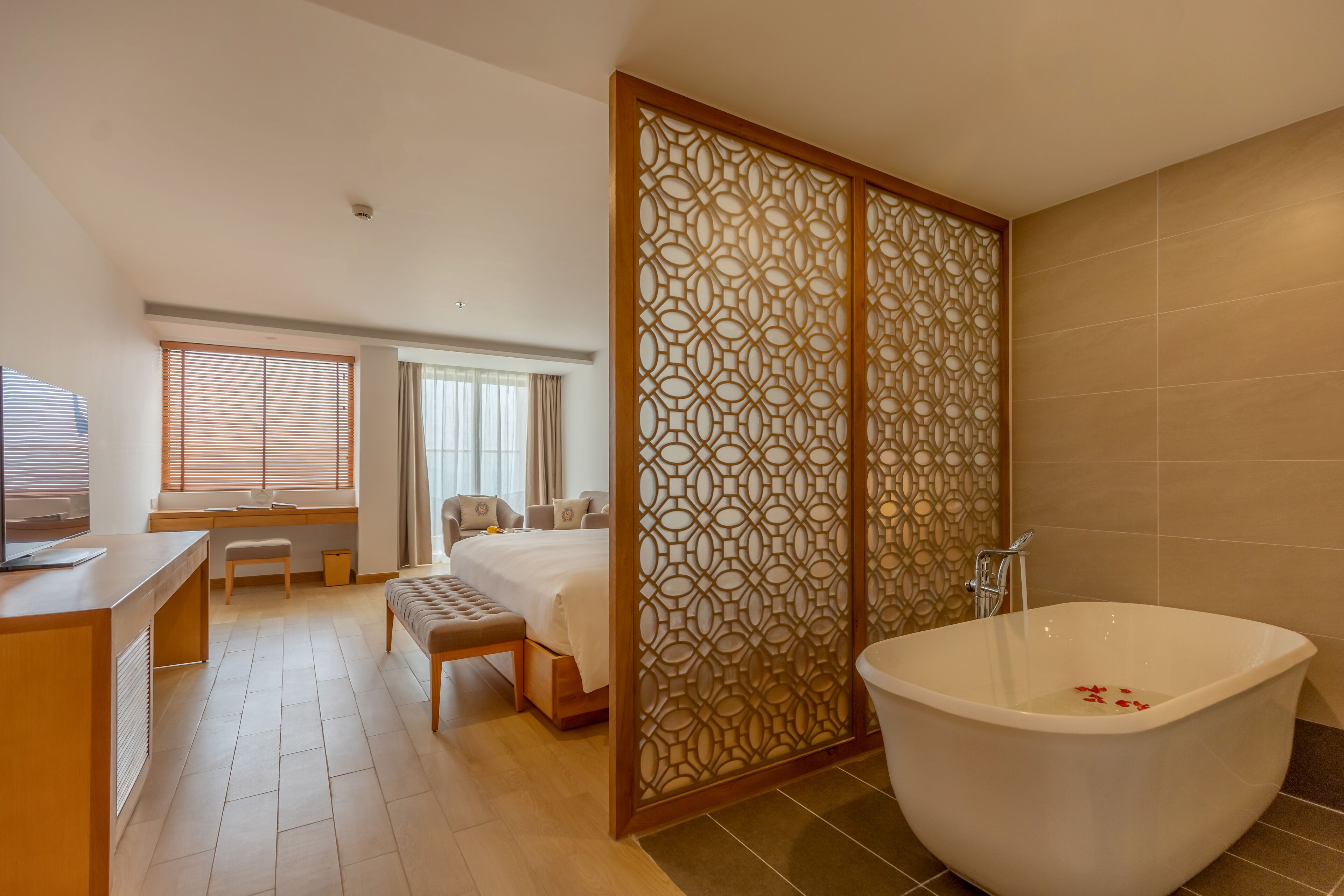 A hotel room with a large bathtub, a desk with a chair, a bed, and a window with blinds.