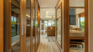 A modern hotel corridor with wooden flooring, glass doors, and a view of a bedroom with a bed, bedside table, and a window.
