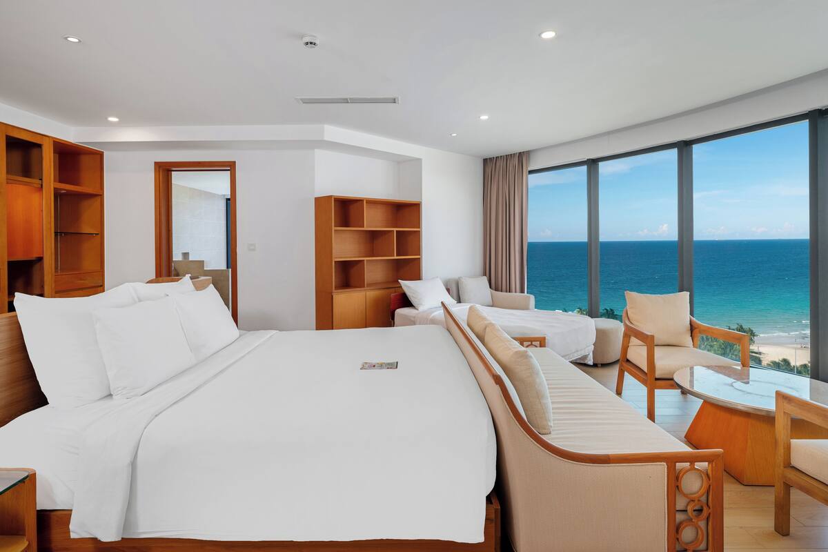 Une chambre d’hôtel moderne dotée d’un grand lit, d’un coin salon et offrant une vue sur l’océan.