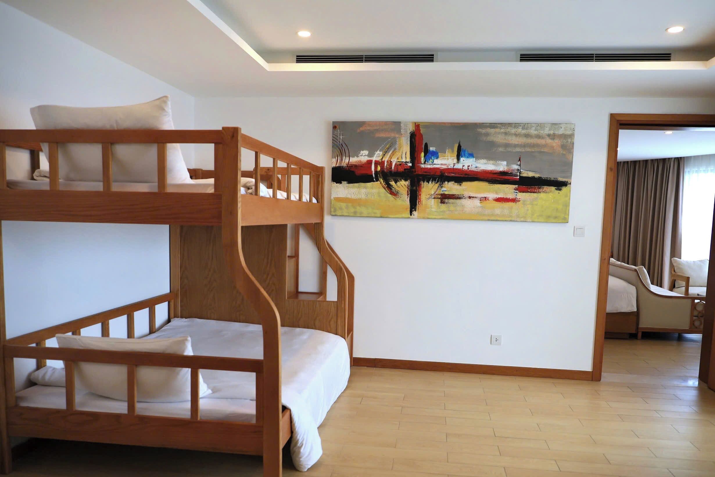 A room with a bunk bed, a painting on the wall, and a chair in the corner.