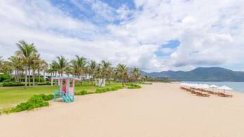 A beach with a lifeguard tower, palm trees, and beach chairs.