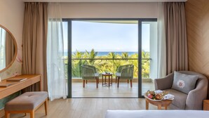 A hotel room with a balcony, a desk, a chair, a sofa, and a small table with a tray of fruit.