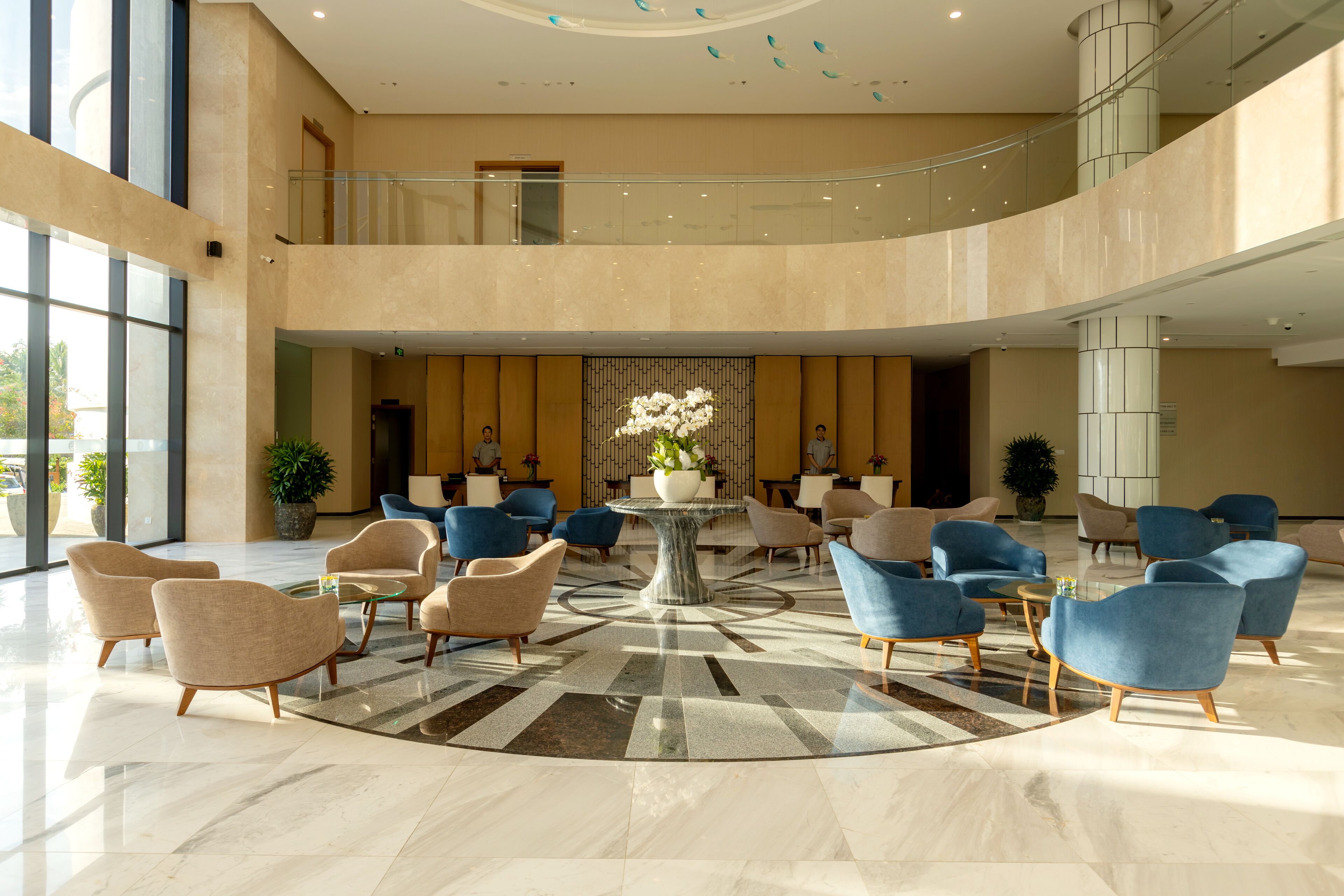 A spacious lobby with a central round table, multiple seating areas, and a high ceiling with decorative elements.