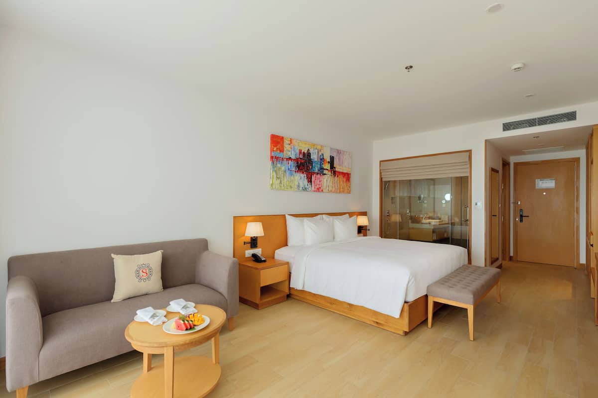 Une chambre d’hôtel avec un lit, un canapé, une petite table avec des fruits et un tableau au mur.