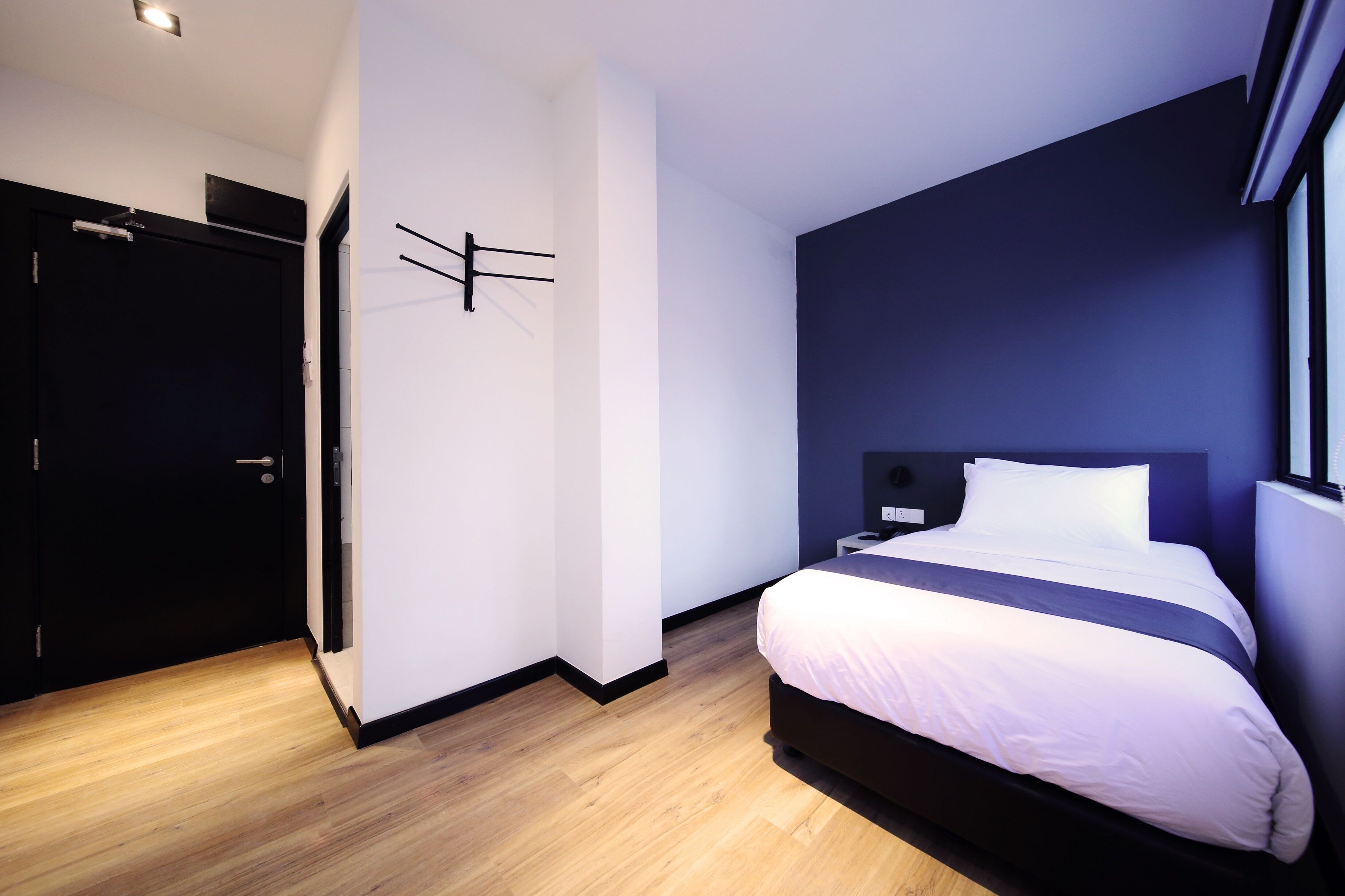 Una habitación de hotel moderna con una cama grande, una pared de acento azul oscuro y suelo de madera.