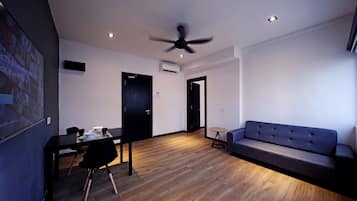 A modern living room with a dark sofa, a dining table with chairs, a ceiling fan, and a small round table.